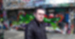 Portuguese DJ and producer Joshua standing in a street with graffiti on the walls looking over his right shoulder at camera and wearing a leather jacket, colour image.