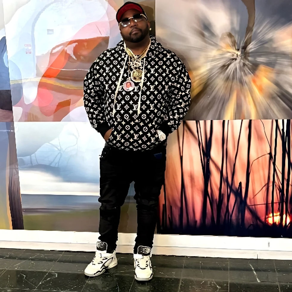 Fuego Base standing full-length against an abstract art wall, wearing a patterned black hoodie, dark jeans, white sneakers, sunglasses, and a red cap in a birthday portrait.
