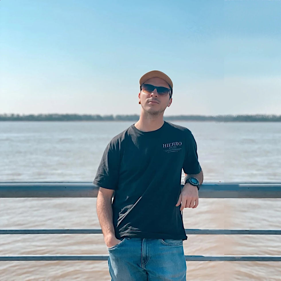 Argentinian DJ and producer Marco Boarelli leaning on a rail beside a river wearing sunglasses and looking at the camera, colour image.