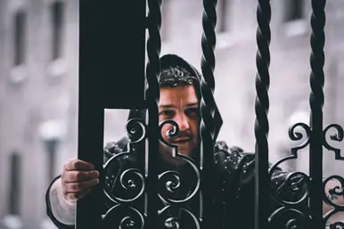 Portrait of Canadian DJ Spiritual Viking, also known as Trevor Peterson, holding an ornate metal gate in rainy weather, representing his Techno sound and Montreal club background.