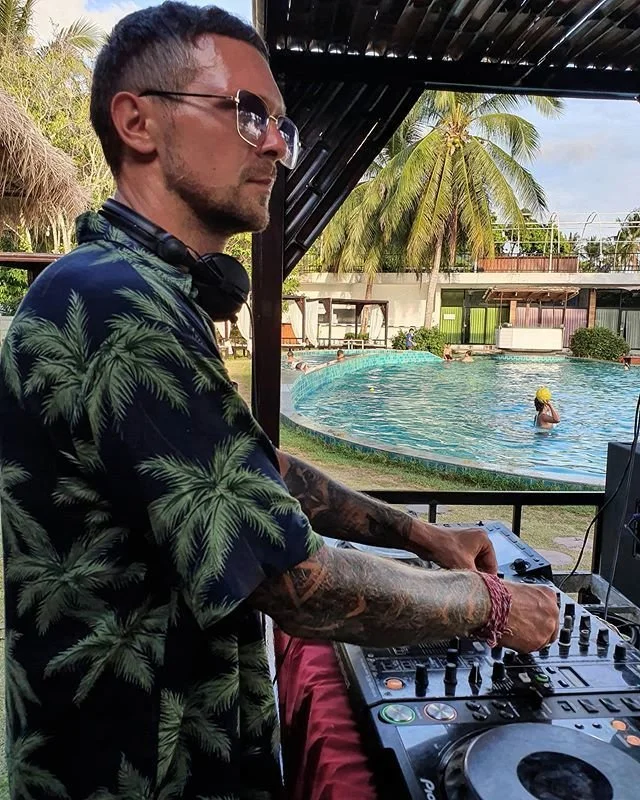 Side shot of Belarusian DJ Igor Hush performing at an outdoor pool party as a DJ in Asia whilst wearing sunglasses.