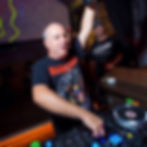 Italian DJ and producer Marco Mei performing at a nightclub and looking at the crowd with his left arm up, colour image taken from his right side.