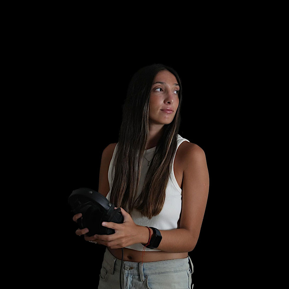 Argentinian DJ and producer Lulu Sfeir standing in a hoto studio with a black background holding her headphones to her front and looking over to the left, colour image.