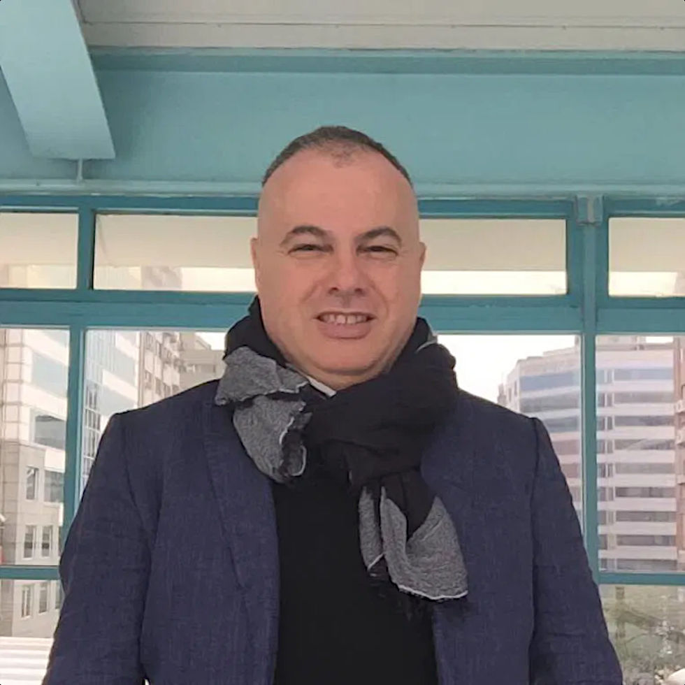 Italian DJ and Producer Marco Mei Wearing a jackets and a scarf round his neck standing the the hallway of a building, colour image.