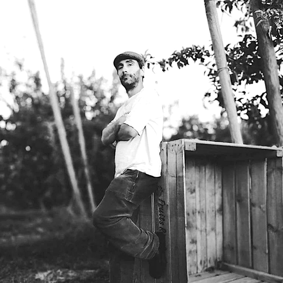 Spanish DJ and producer A503X standing with arms crossed leaning on a box, black and white image.