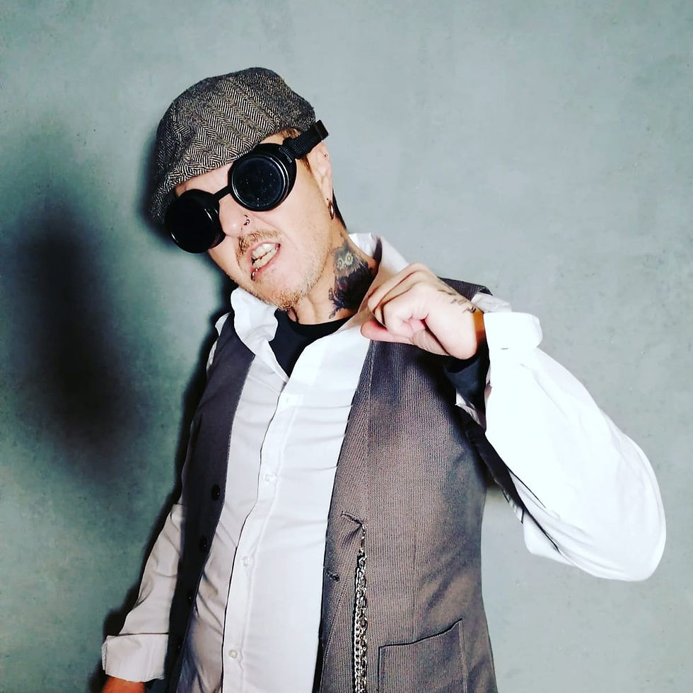 Italian DJ and producer El Brujo wearing a hat and goggles with left fist raised in upper body shot, colour image.