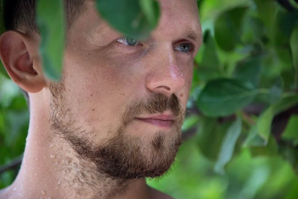 belarusian Dj Igor Hush stading in bushes with his face visible from the right side, colour image.