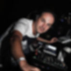 Marco Mei wearing headphones while performing at a club DJ setup with a mixer and laptop.