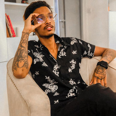Sri Lankan DJ and producer Nikhila Hashen sitting in a chair holding his glasses with his right hand and looking upwards, facing left slightly, colour image