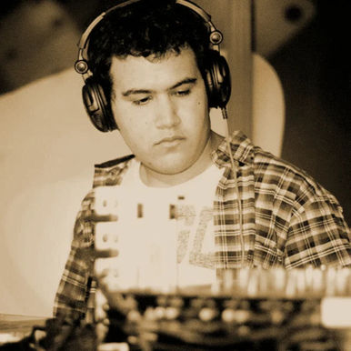 Jero Nougues focused at the decks wearing headphones, in a sepia-toned shot.