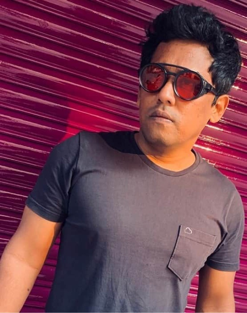Indian DJ and producer Psy Inertia leaning against metal shutters and wearing sunglasses, colour image.