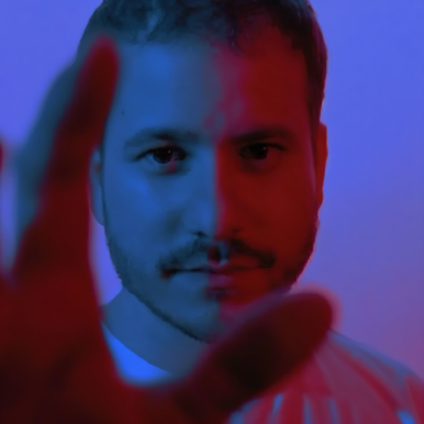 Argentinian DJ and producer Byhon standing with his hand open in front of him and looking through his thumb and forefinger in a chromed pink and blue shot, colour image