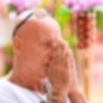 British DJ and producer Graham Gold with his hands together in a prayer gesture, wearing glasses on his head and standing outdoors.