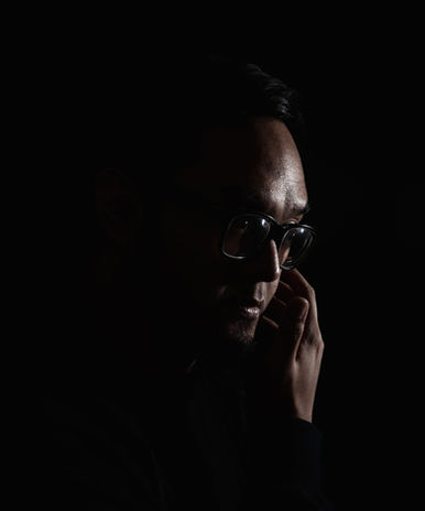 Indonesian DJ Yorri in dark room right side of face showing with right hand on left cheek, colour image.