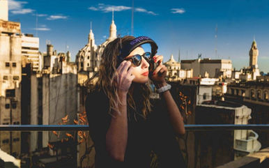 Argentinian DJ and producer Bodai performing on a rooftop in Buenos Aires, facing her left with headphones held in both hands, and city buildings visible in the background in a colorful image.