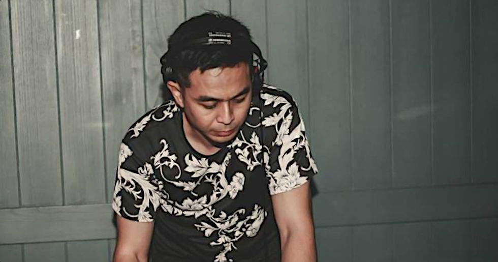 Malaysian DJ and producer Hadiid performing at an event leaning over CDJ's, colour image.