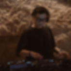 Malaysian DJ and producer Terence C stands at the turntables and mixer at Bam Bam, looking straight ahead, a shadow cast on the right side of his face. He sports thick-rimmed Ray-Ban glasses and a black T-shirt in a vibrant color image.