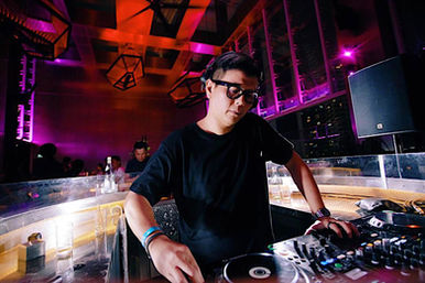 Malaysian DJ and producer Terence C is performing at Wet Deck in Kuala Lumpur, wearing a black T-shirt. In the color image, he’s captured from the front, fully focused on the CDJs and mixer.