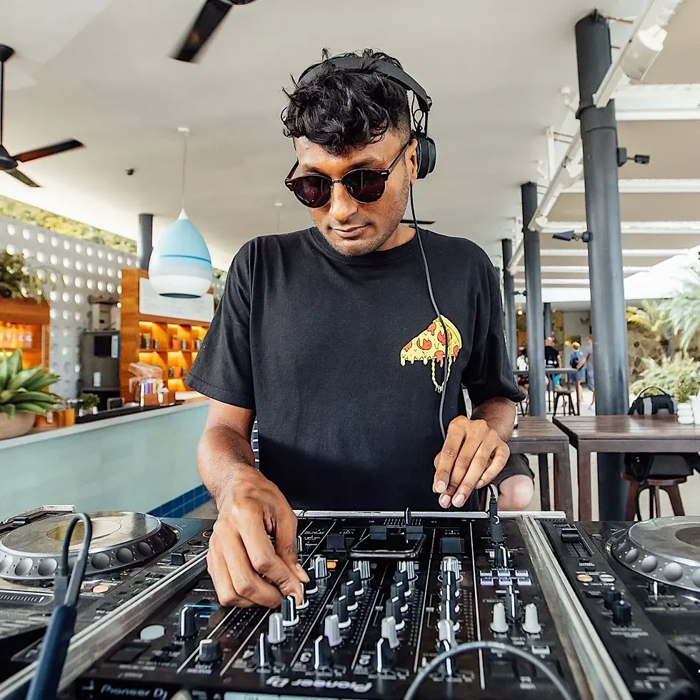 Sivanesh, Singapore-based house and techno DJ, performing on Pioneer DJ equipment at an open-air daytime bar venue wearing sunglasses and headphones.