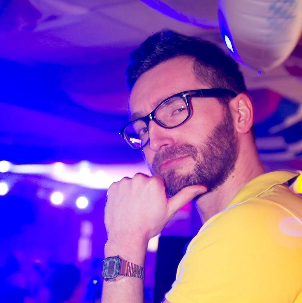Italian DJ and producer INVE looking over his left shoulder with his hand on his chin wearing glasses, colour image.