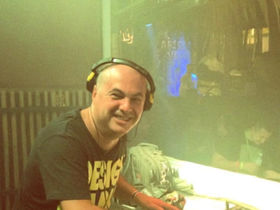 Italian DJ and producer Marco Mei performing at an event wearing headphones and looking at the cameraman with his hands on the CDJs, colour image.