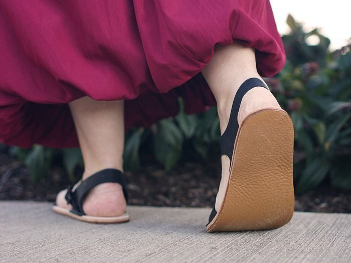 person walking away from the camera, low angle shot from the ground. They are wearing black sandals with a strap around the back of the heel.