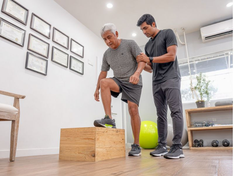 Senior adult practicing balance exercises with supportive Filipino physical therapist in bright clinic
