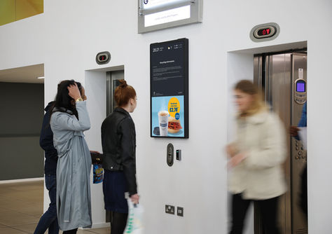 Students staring at a Greggs ad on a lift screen