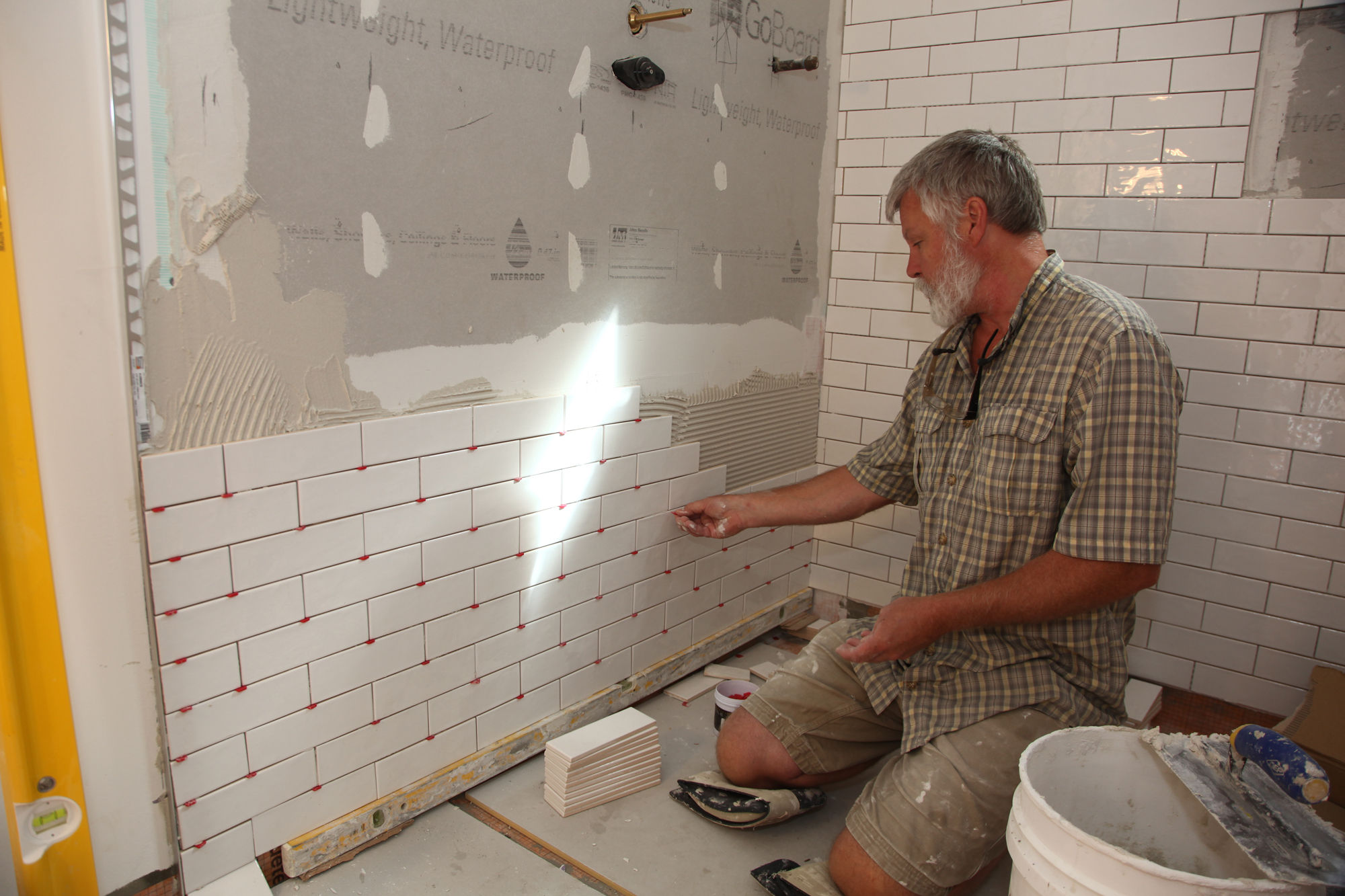 Man installing white tiles on a wall, Trim Work, home repair services in progress.
