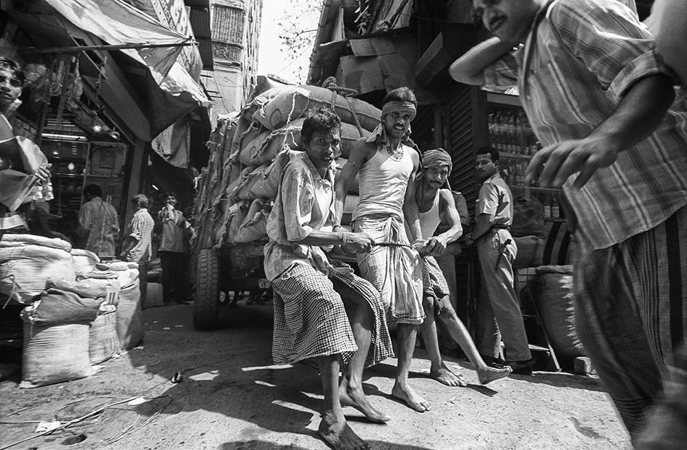 Cart pullers struggle with an overloaded cart in Burrabazar, Kolkata, India.