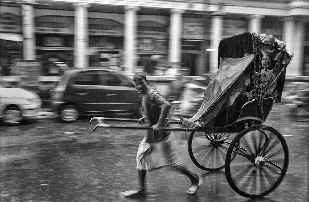 A rickshaw puller carries passengers through the streets of Kolkata under heavy monsoon rain.