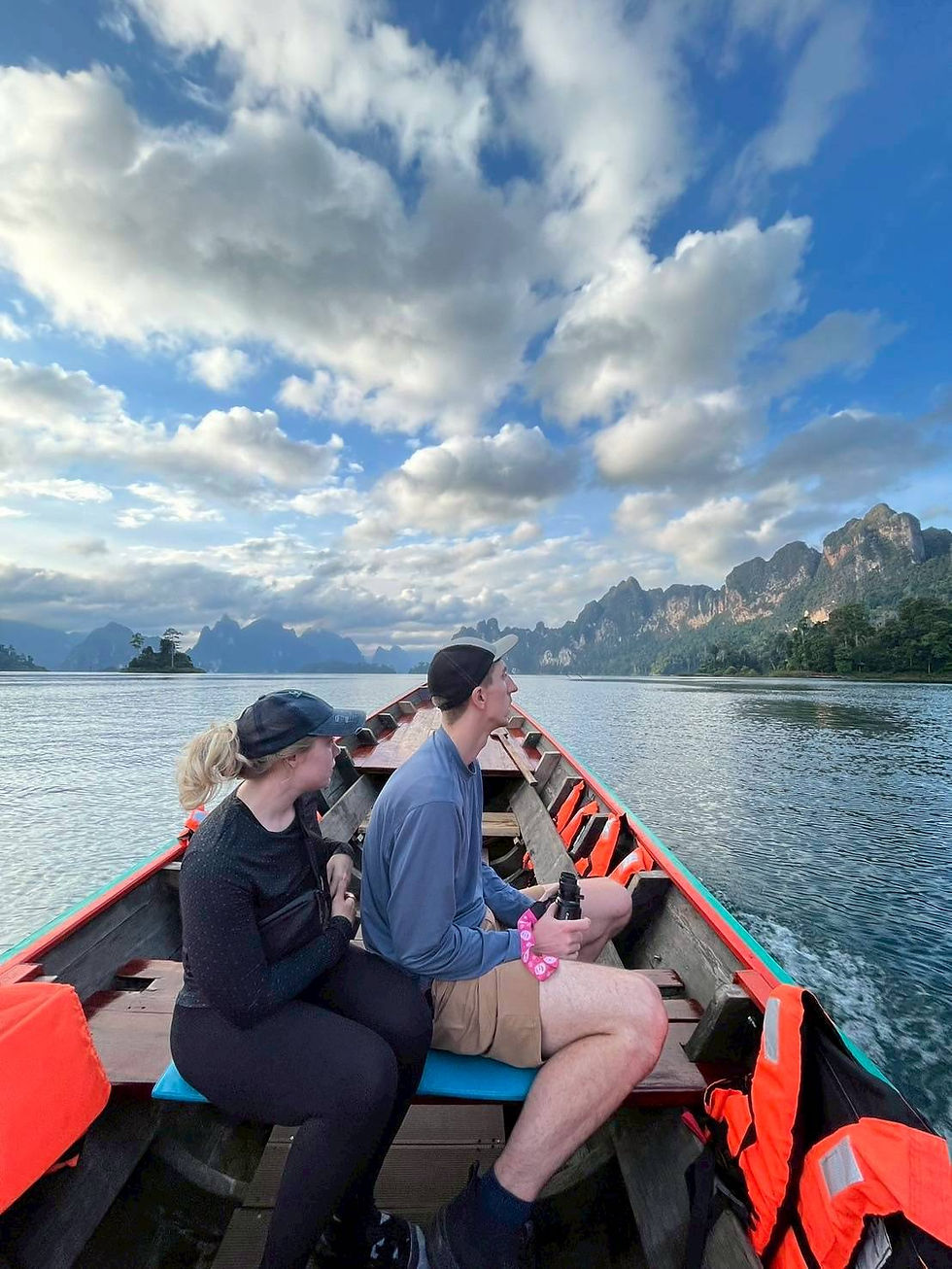 Two visitors seated in a longtail boat beneath a cloud-filled sky