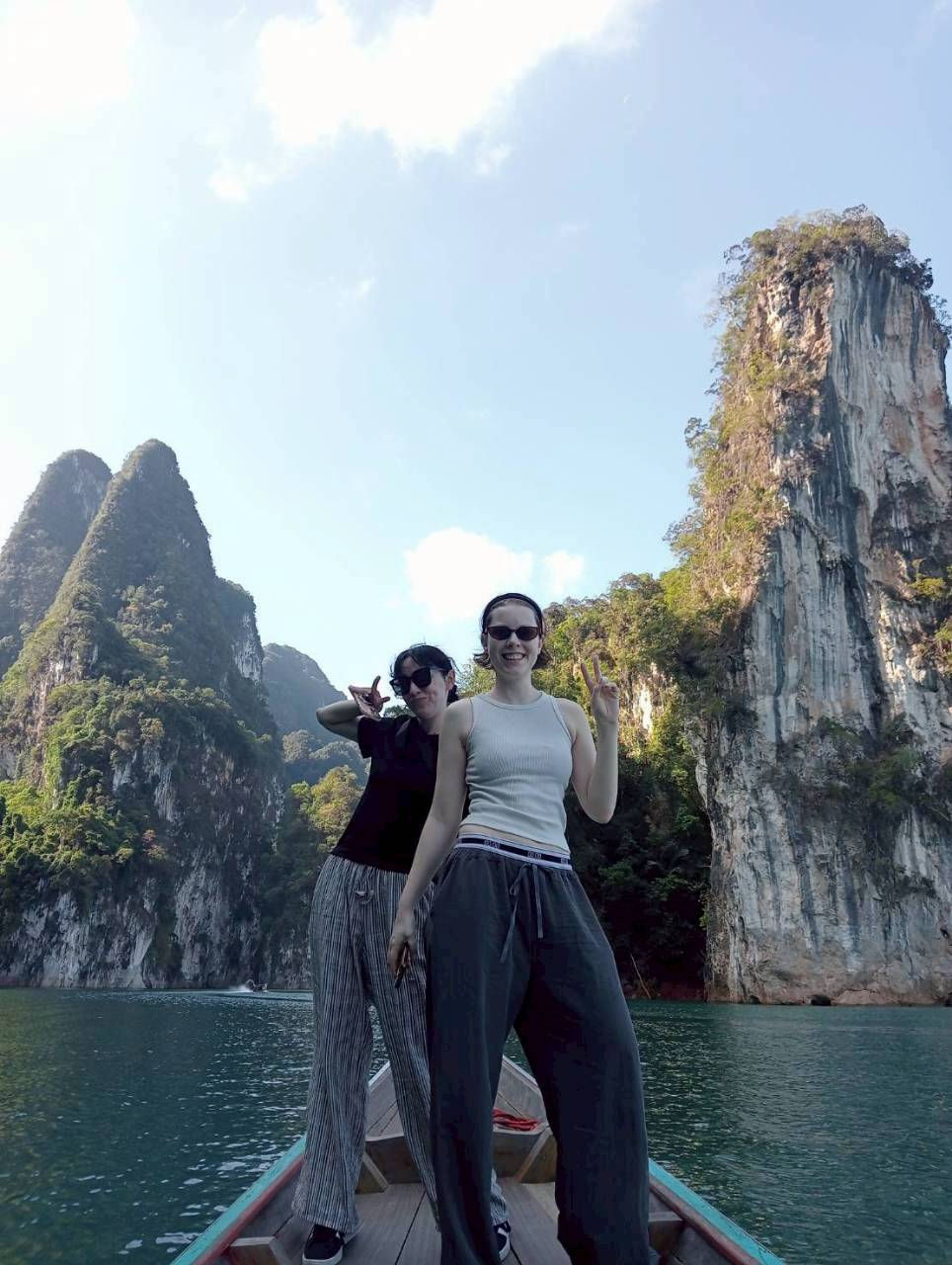Two guests standing at the boat bow beneath limestone cliffs