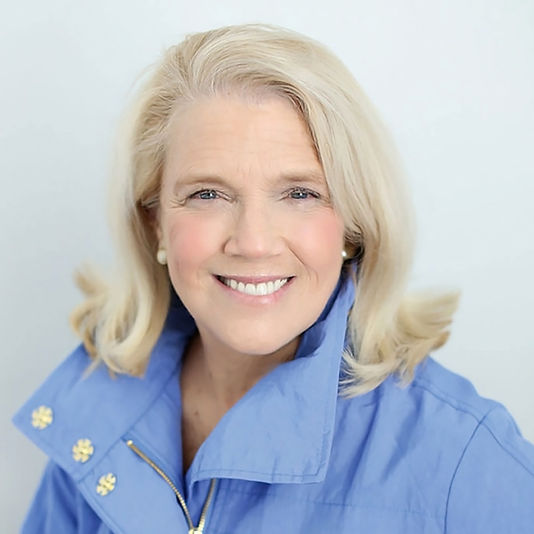 Sharon Heflin smiles at the camera. She has shoulder length blonde hair, and blue eyes. She wears pear earings and a light blue jacket.