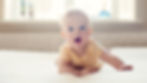 Blue eyed infant in a yellow shirt crawling on the floor