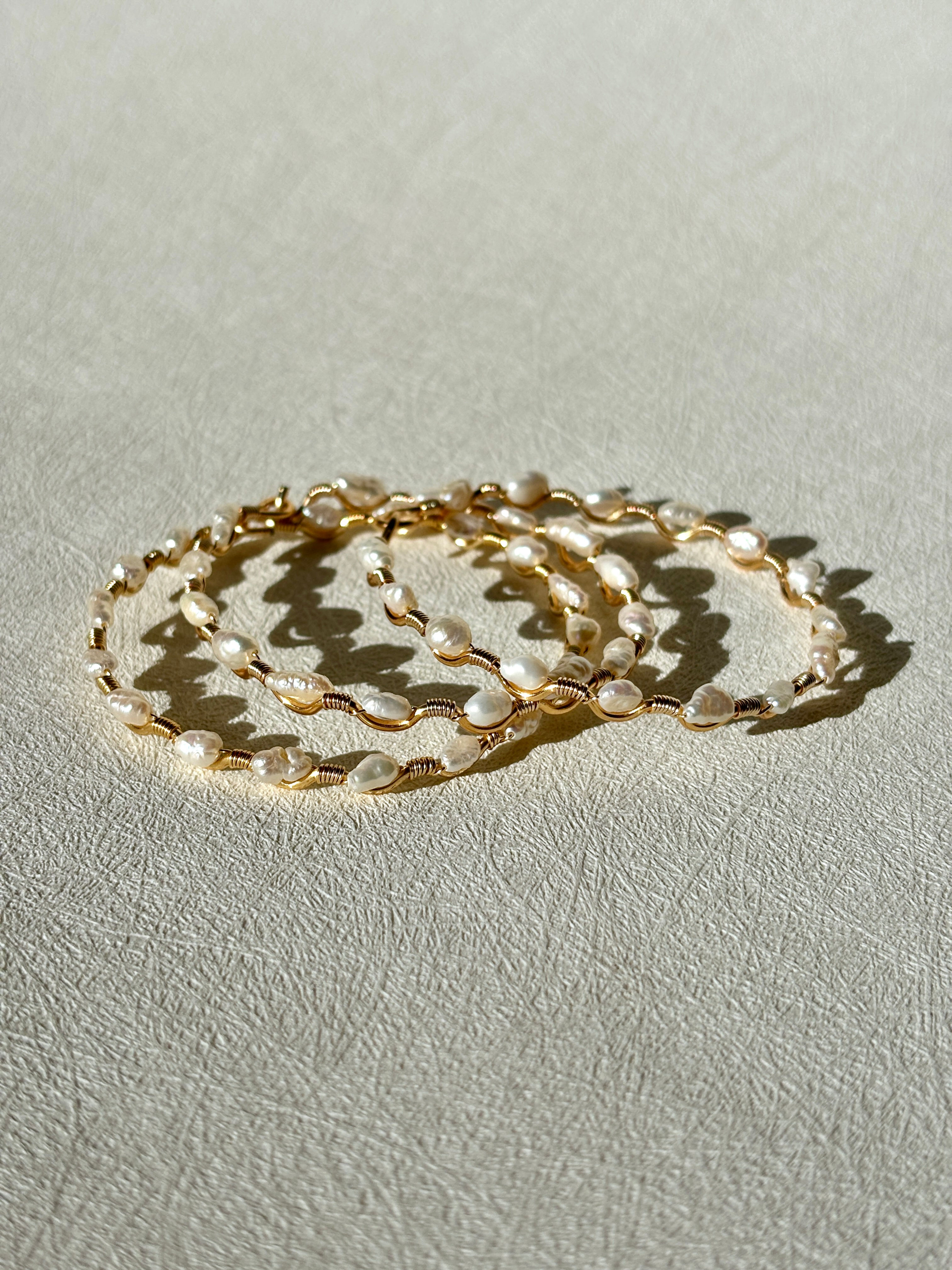 Three Pearl Paloma Bracelets stacked on a textured surface