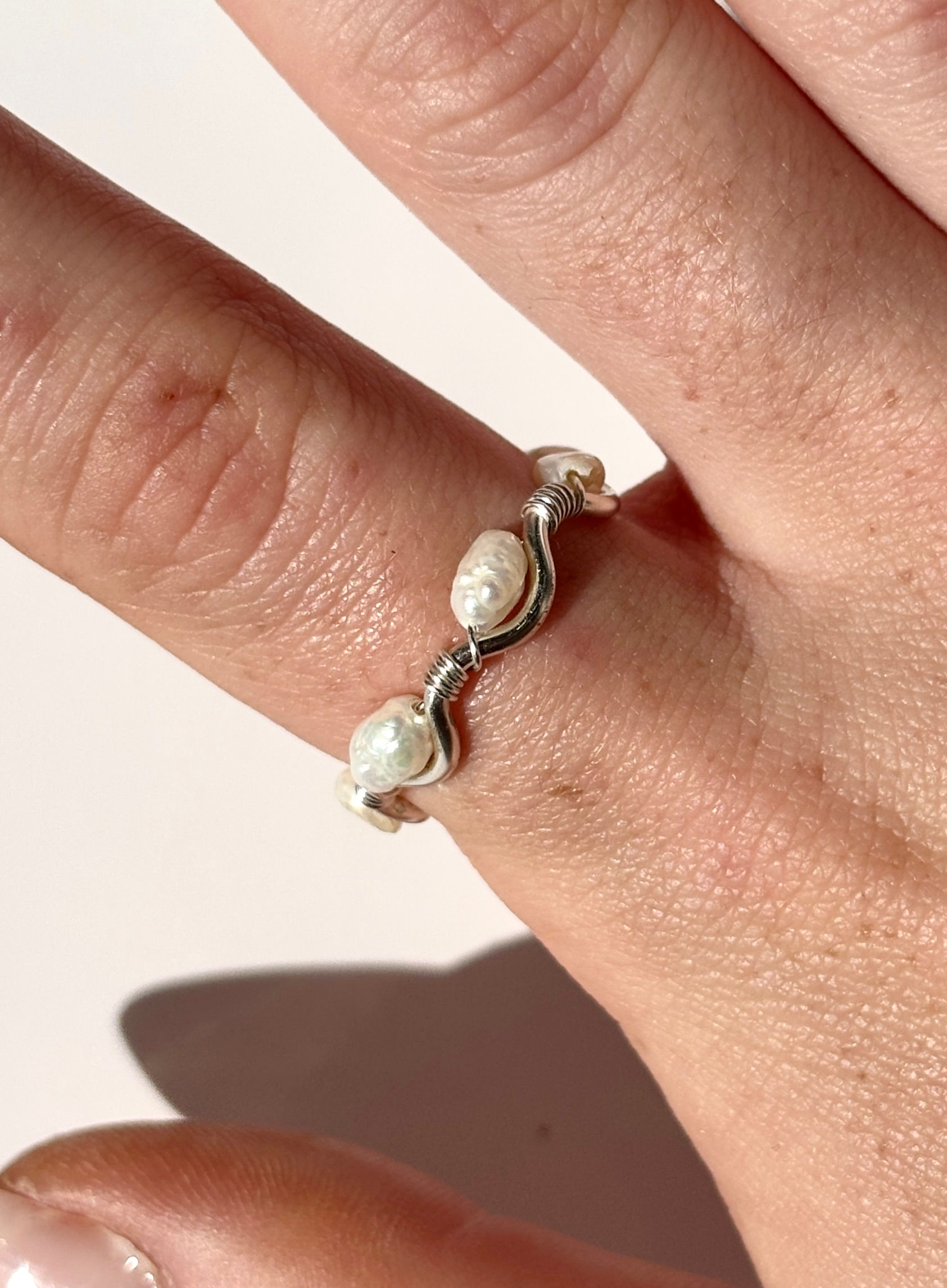 Silver wavy ring with three small pearls on a finger.