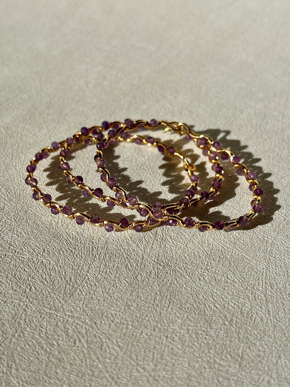 Three Amethyst Paloma Bracelets with purple beads and gold wire.