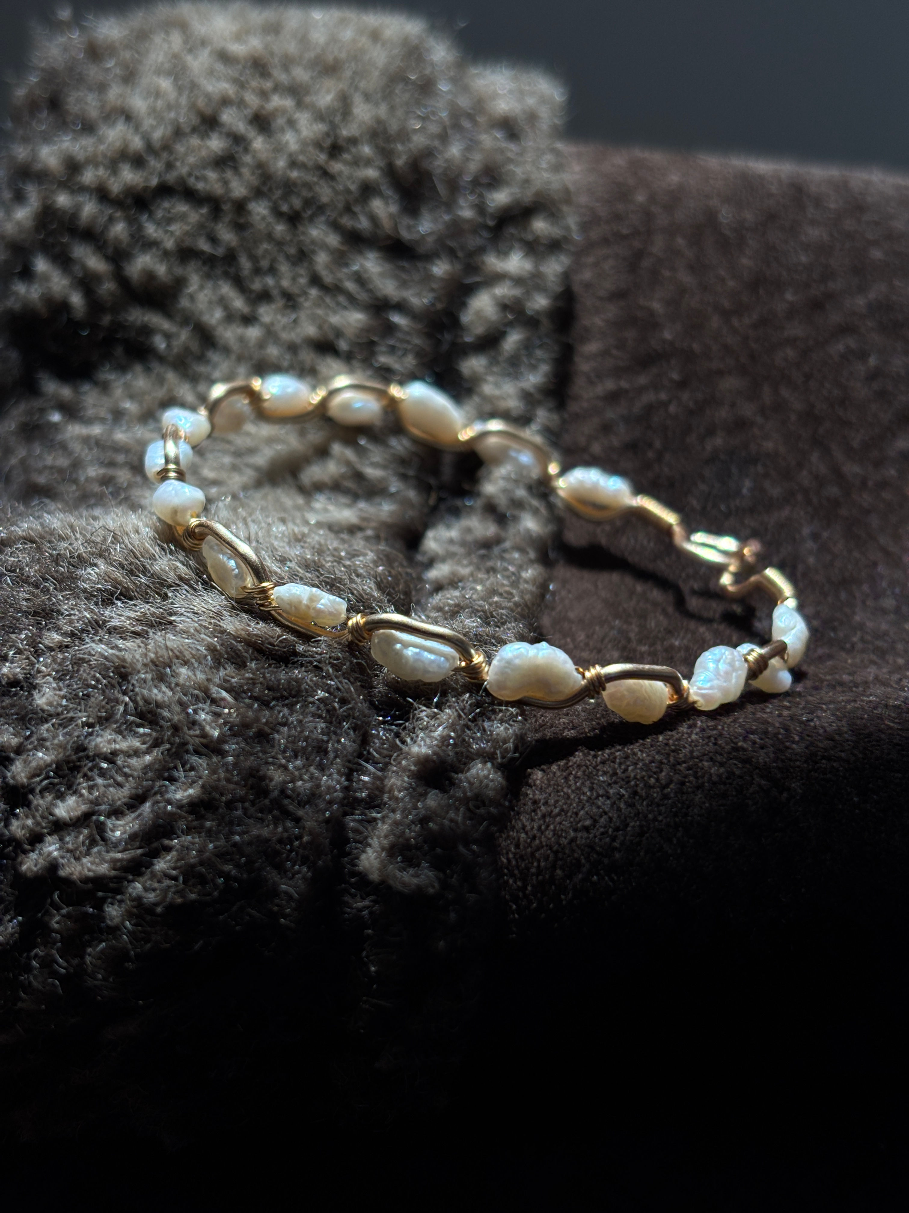 Gold and pearl Paloma bracelet on a textured fabric.