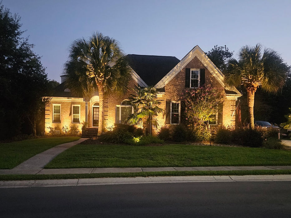 Illuminated brick house with palm trees at dusk.
