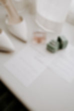 White heels, pink perfume, and rings in a green box on a table with wedding invites for Katherine and Harry, under soft lighting. Elegant mood.