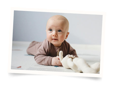 Baby laying on tummy propping themselves up by their elbow and holding a stuffed rabbit.