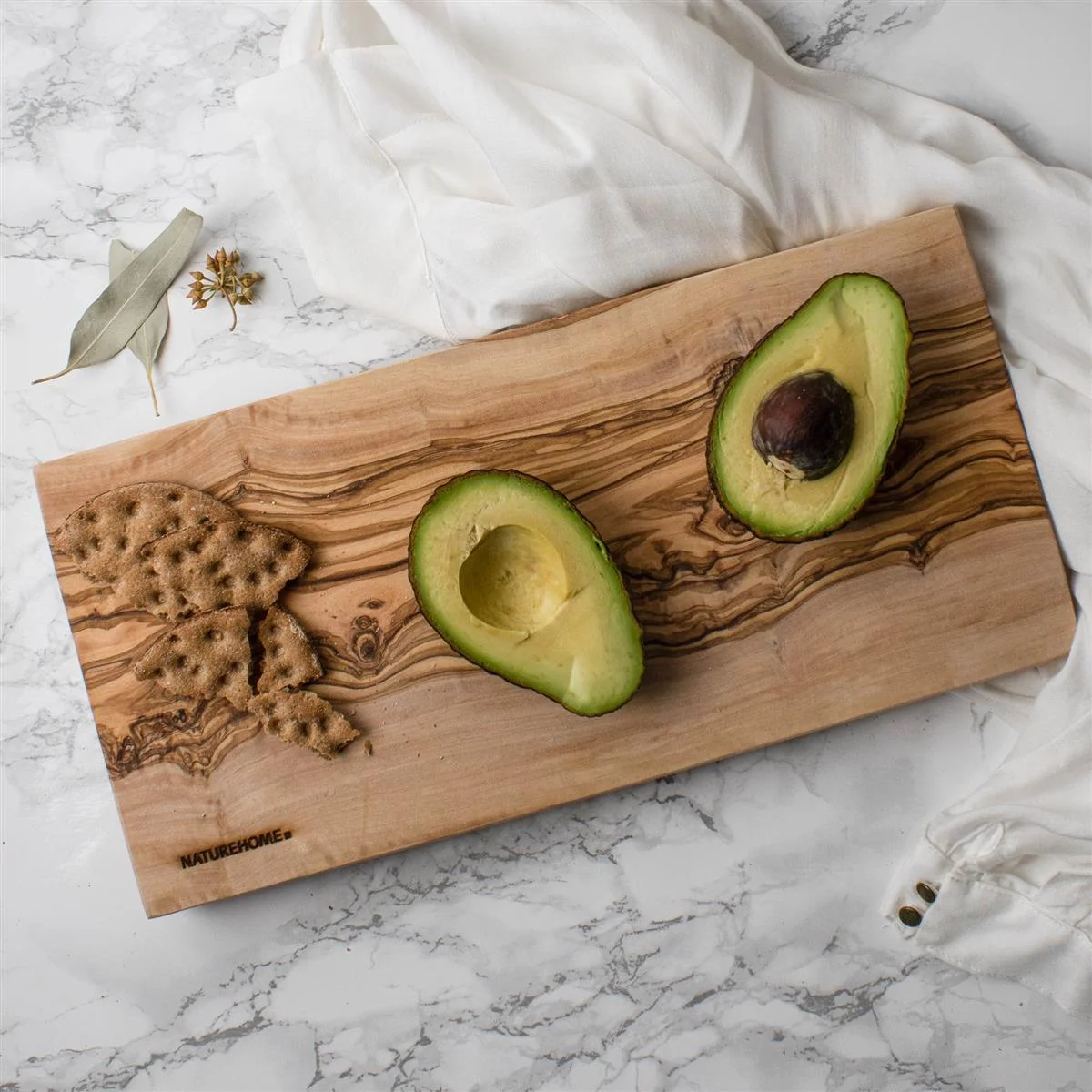 Schneidebrett aus massivem Olivenholz mit Avocado und Knäckebrot als Beispiel für hochwertiges, nachhaltiges Küchendesign.