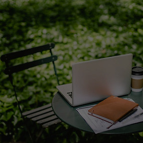 Zu sehen ist ein Laptop auf einem Gartentisch und ein Stuhl