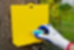A person wearing gloves, refilling a yellow Vespex bait station, that is screwed into a tree, with blue bait.