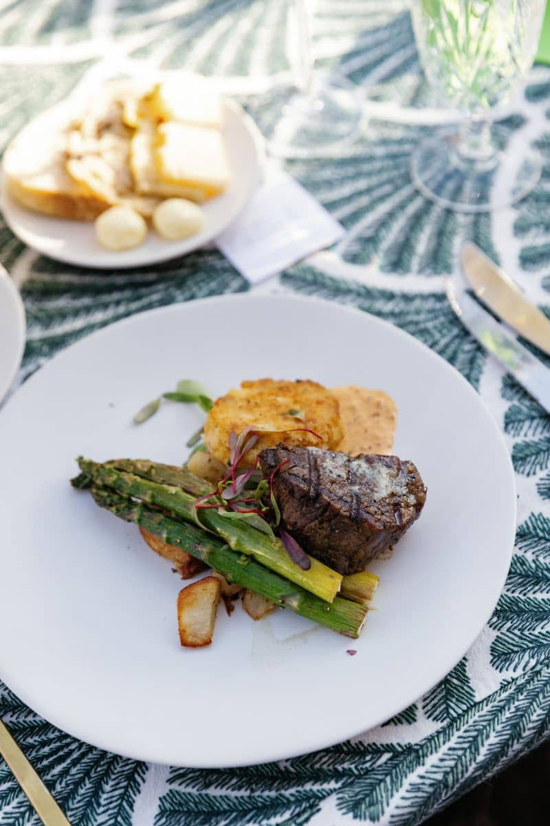 A beautifully plated dish featuring a grilled filet mignon, asparagus, and roasted potatoes, garnish