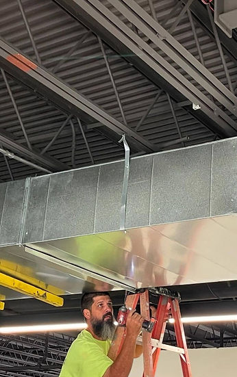 ClimateMakers technician securing metal ductwork to the ceiling at a commercial site in Charleston, SC, highlighting expertise in HVAC system installation for businesses in Mount Pleasant, Summerville, and Goose Creek