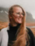 Eine Frau im Profil, aufgenommen in Island mit einem Berg und Nebel im Hintergrund. Das Bild zeigt sie lächelnd.
