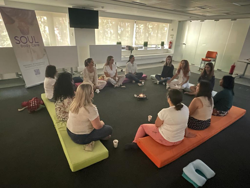 Grupo de mulheres sentadas em roda, com uma das mulheres no centro a explicar as terapias