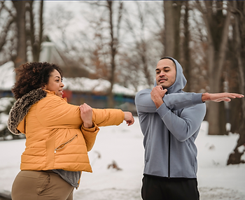 Getting ready for a winter workout, two people stretch together in a snow-covered park.